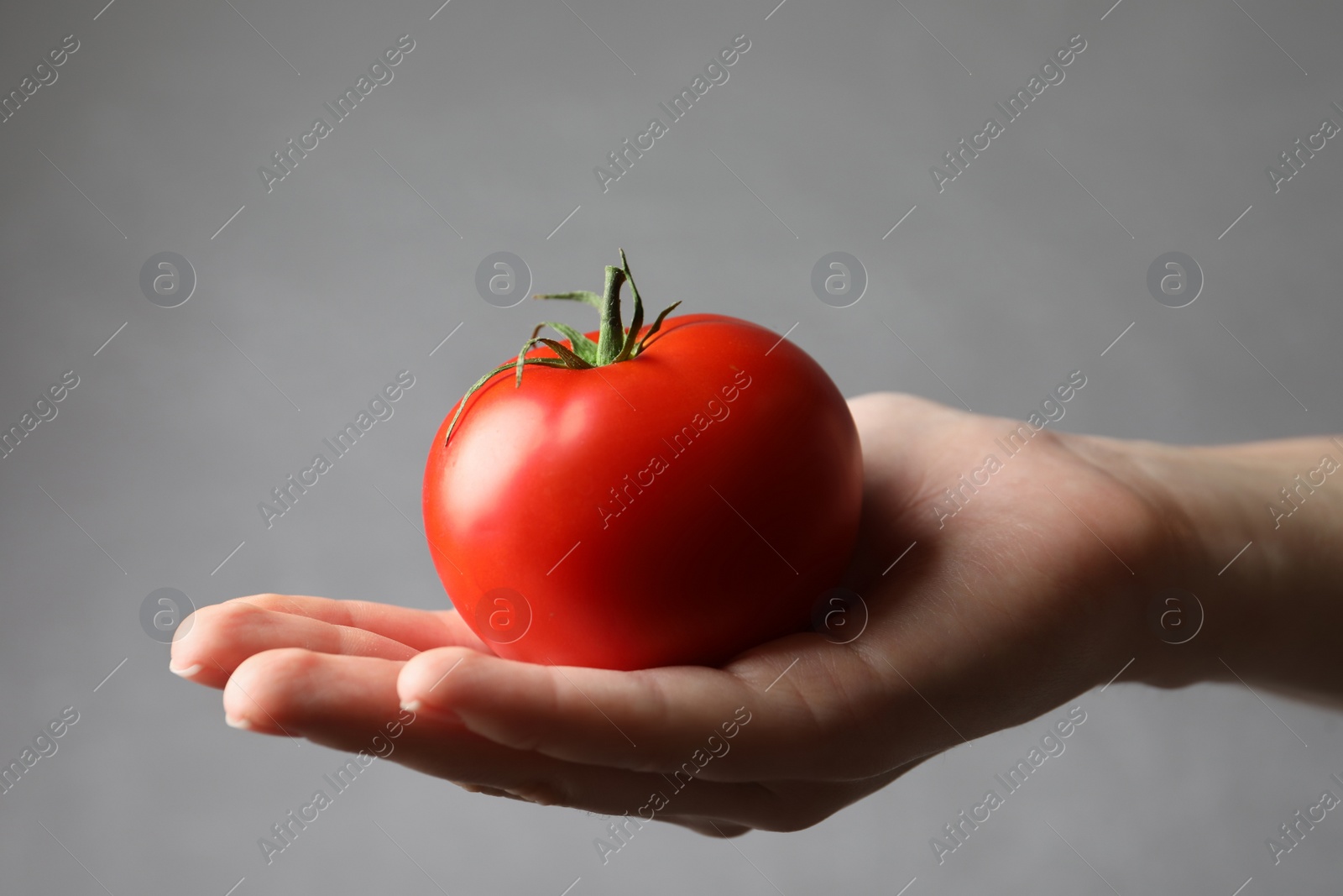 Photo of Woman with ripe tomato on grey background, closeup