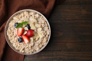 Photo of Tasty oatmeal with strawberries, blueberries and almond flakes in bowl on wooden table, top view. Space for text