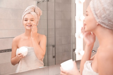 Beautiful woman with clean towels applying face cream in bathroom