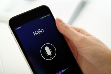 Photo of Woman using voice search on smartphone against blurred background, closeup