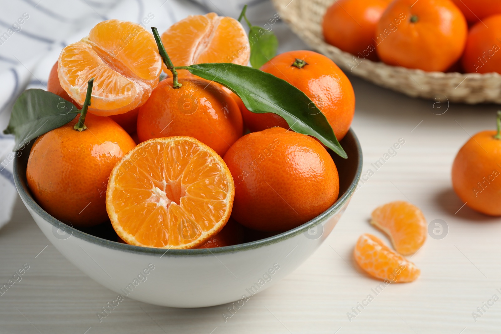 Photo of Delicious tangerines with green leaves in bowl on white wooden table, closeup