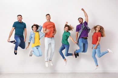 Photo of Group of young people in jeans and colorful t-shirts jumping near light wall