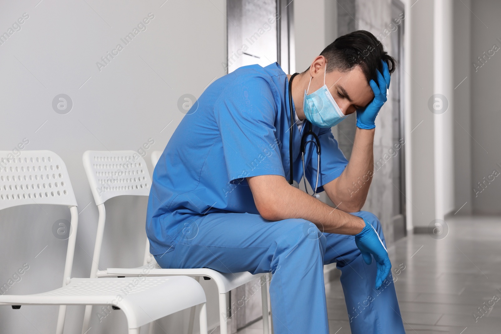 Photo of Exhausted doctor sitting on chair in hospital hallway