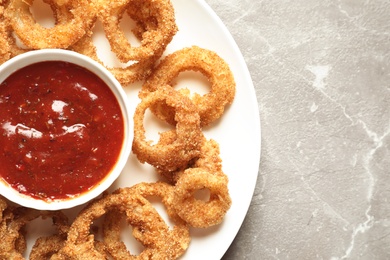 Photo of Homemade crunchy fried onion rings with sauce on color table, top view. Space for text