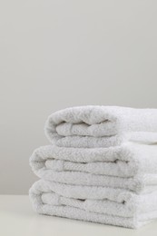 Stack of clean soft white towels on table against light grey background