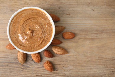 Photo of Delicious nut butter in bowl and almonds on wooden table, top view. Space for text