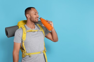 Photo of Happy tourist with backpack drinking on light blue background, space for text