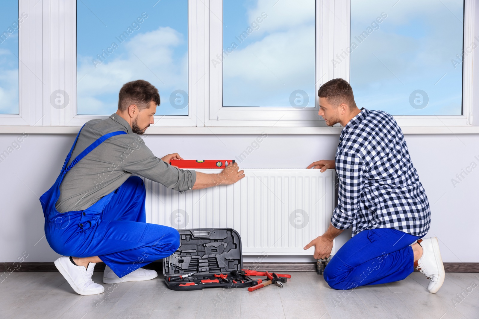 Photo of Professional plumbers using bubble level for installing new heating radiator in room