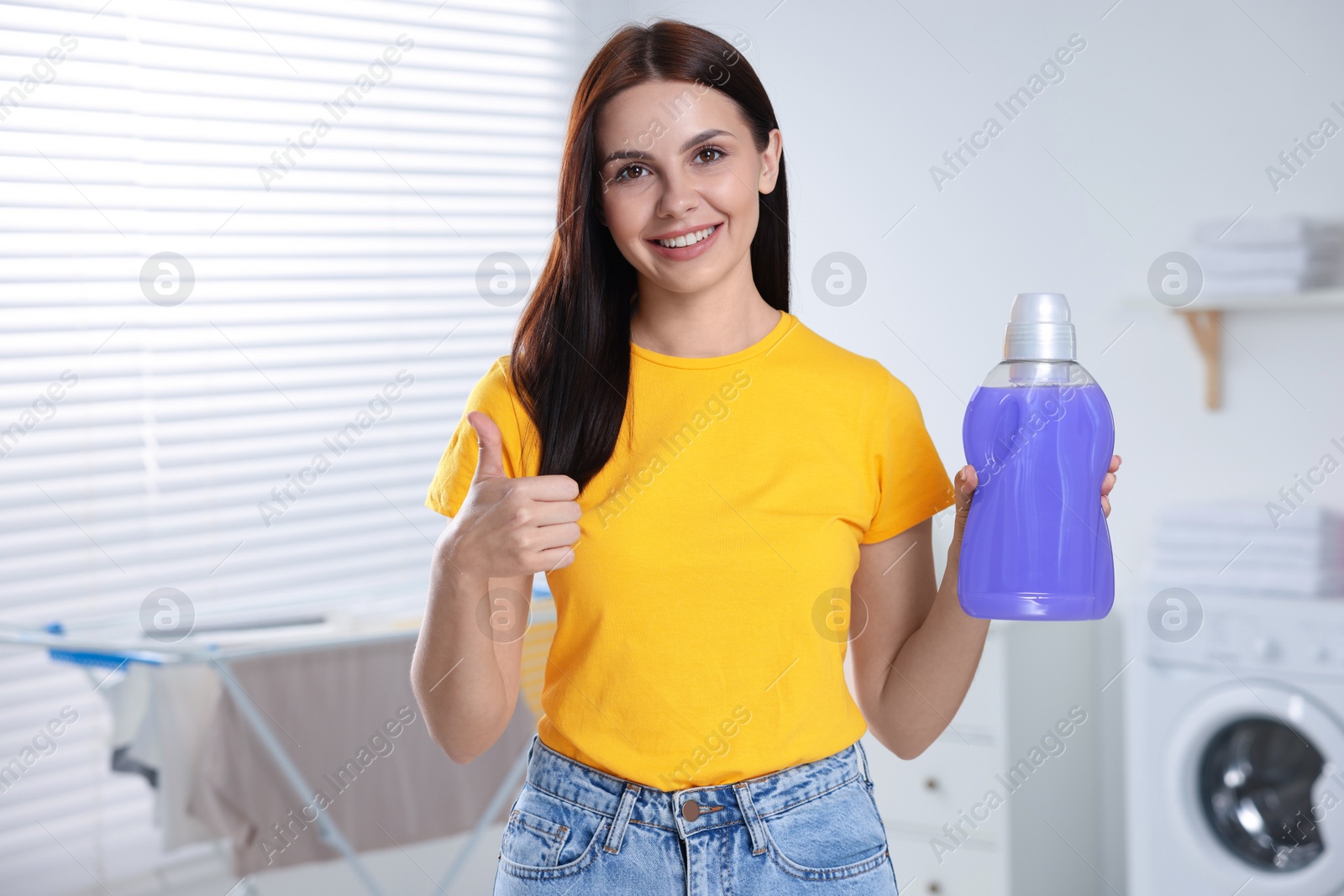 Photo of Woman holding fabric softener and showing thumbs up in bathroom, space for text