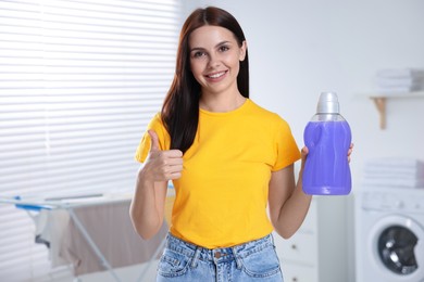 Woman holding fabric softener and showing thumbs up in bathroom, space for text
