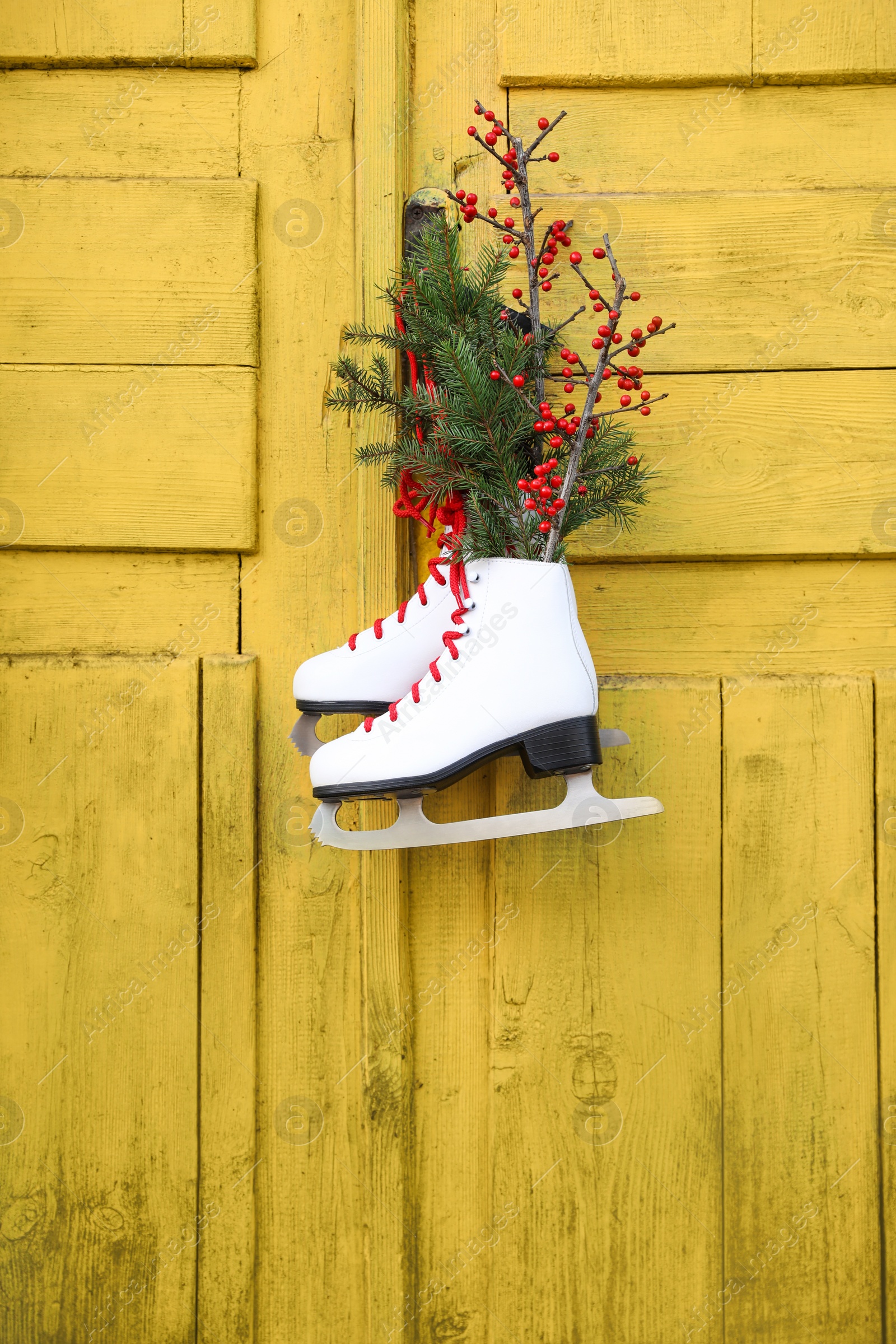 Photo of Pair of ice skates with Christmas decor hanging on old yellow door