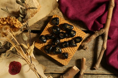 Composition with black rune stones and dried plants on wooden table, flat lay