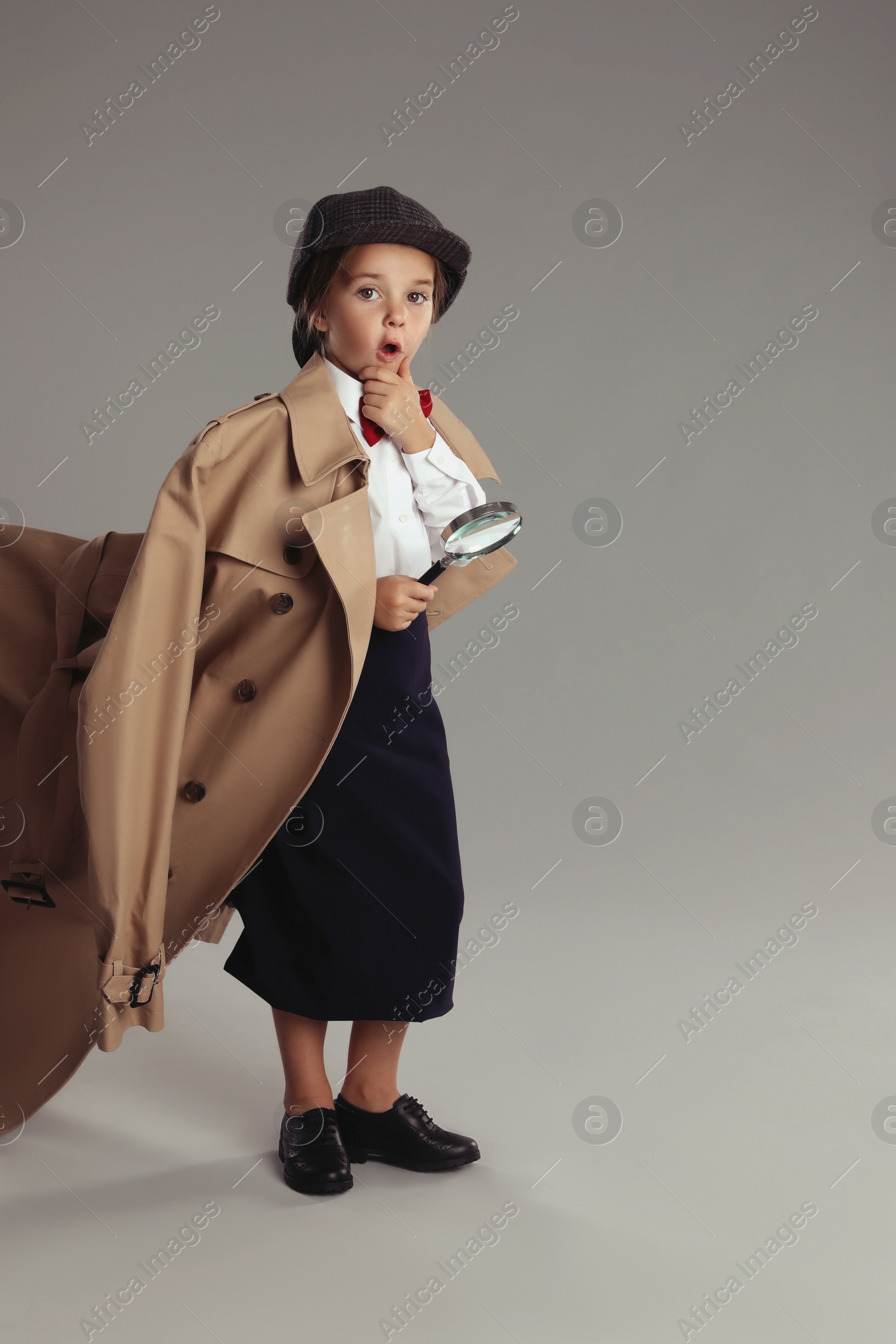 Photo of Cute little child in hat with magnifying glass playing detective on grey background, space for text