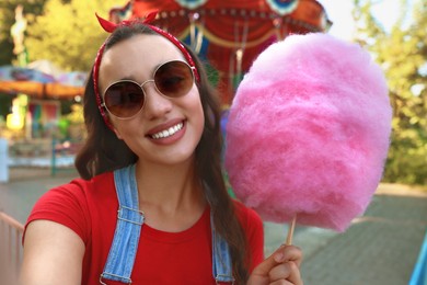 Photo of Stylish young woman with cotton candy taking selfie at funfair