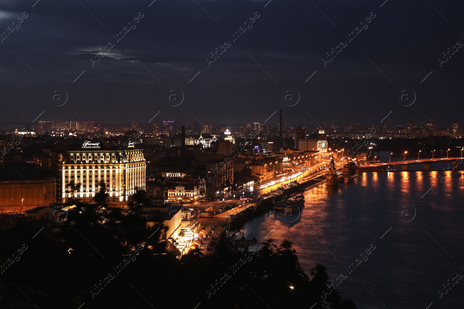 Photo of KYIV, UKRAINE - MAY 21, 2019: Beautiful view of night city with illuminated Fairmont Grand Hotel and other buildings near river