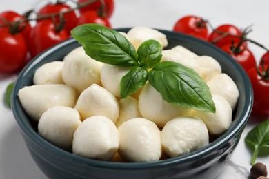 Photo of Delicious mozzarella balls and basil leaves in bowl, closeup