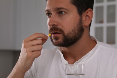 Photo of Depressed man with glass of water taking antidepressant pill indoors, closeup