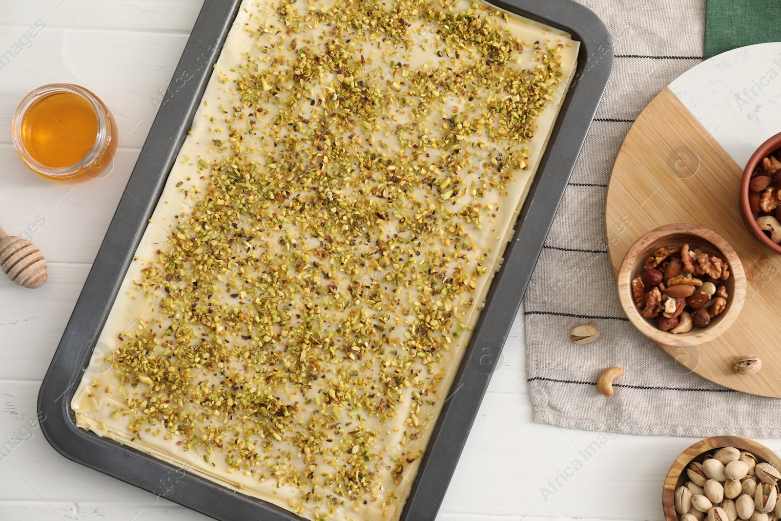 Photo of Making delicious baklava. Baking pan with dough and ingredients on white wooden table, flat lay