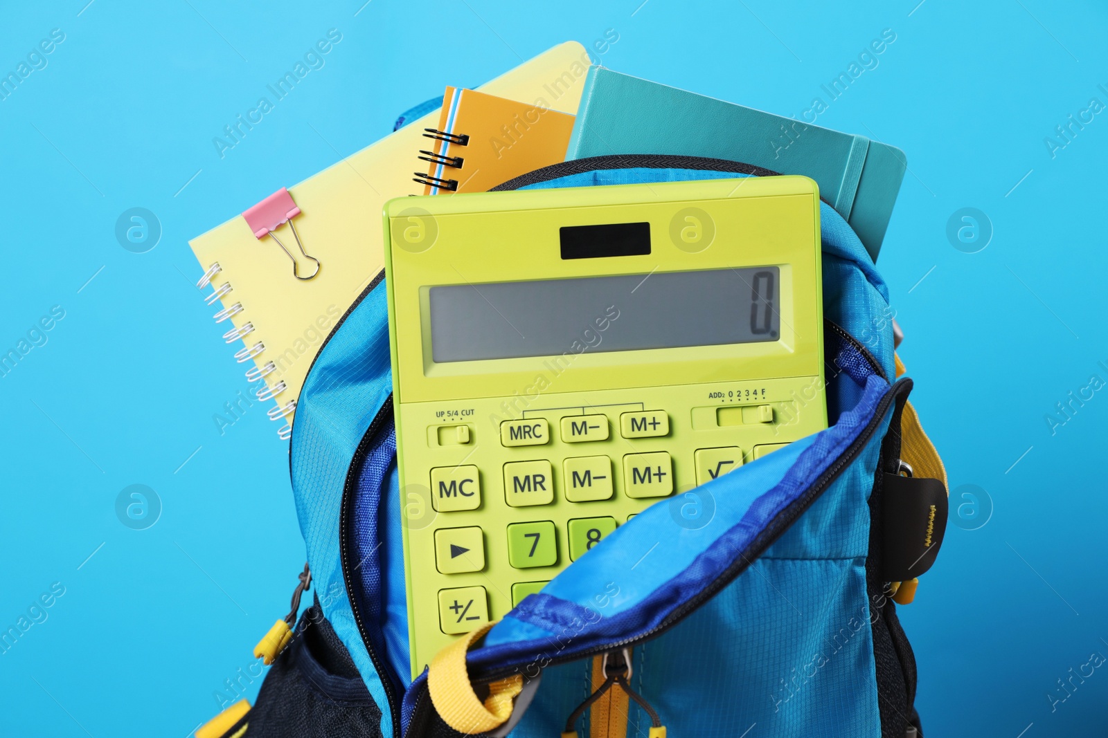 Photo of Backpack with different school stationery on light blue background, closeup