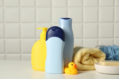 Baby cosmetic products, bath duck, sponge and towel on white table against tiled wall