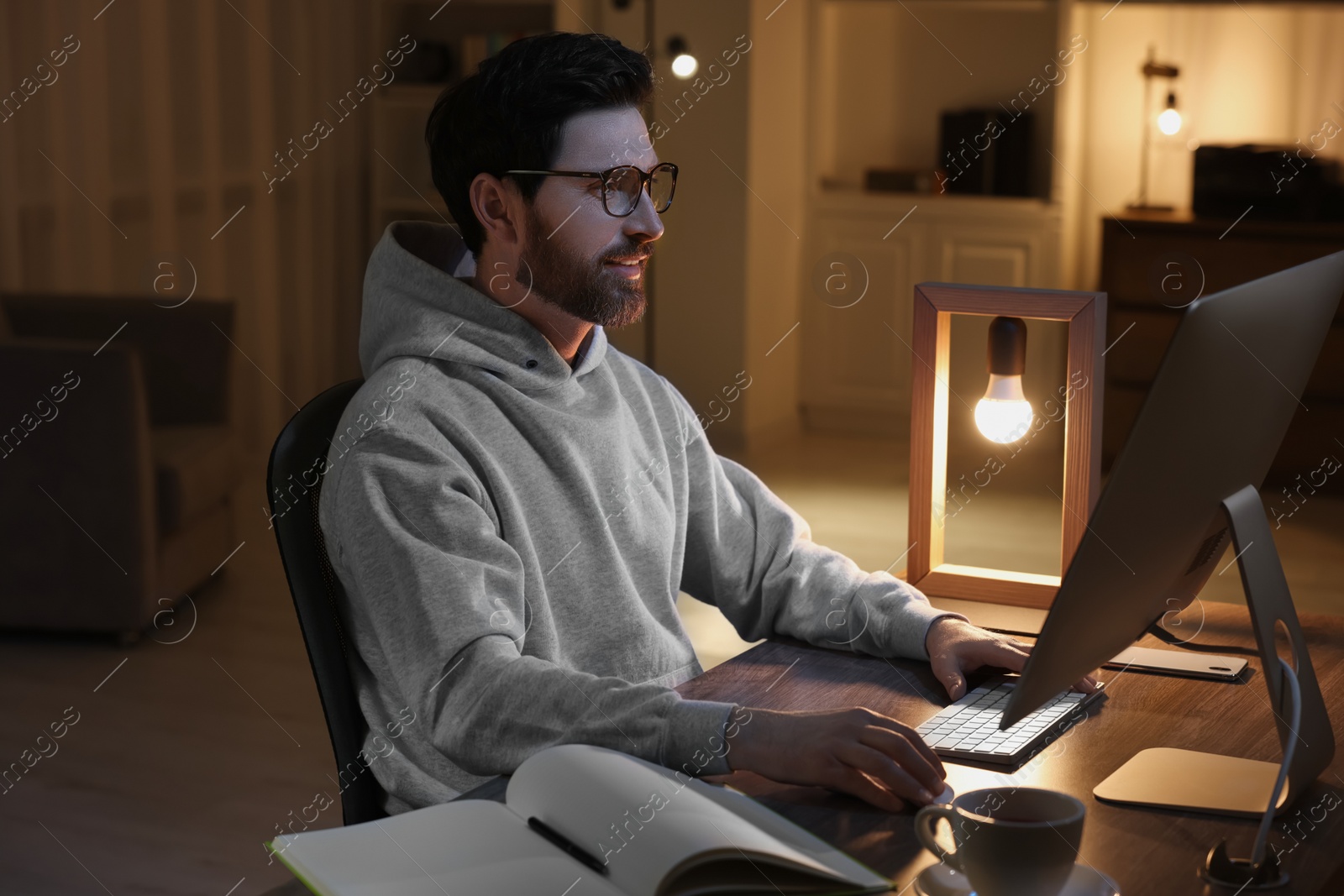 Photo of Home workplace. Man working with computer at wooden desk in room at night
