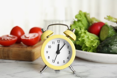 Photo of Alarm clock and vegetables on white marble table. Meal timing concept