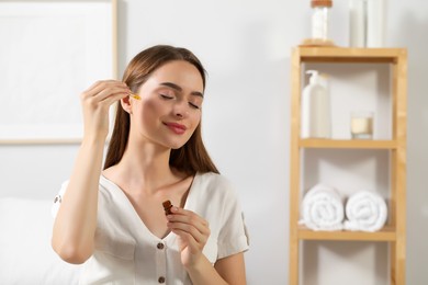 Photo of Young woman applying essential oil onto face at home, space for text