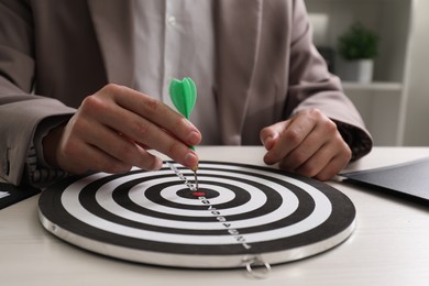 Photo of Business targeting concept. Man with dart aiming at dartboard at table indoors, closeup