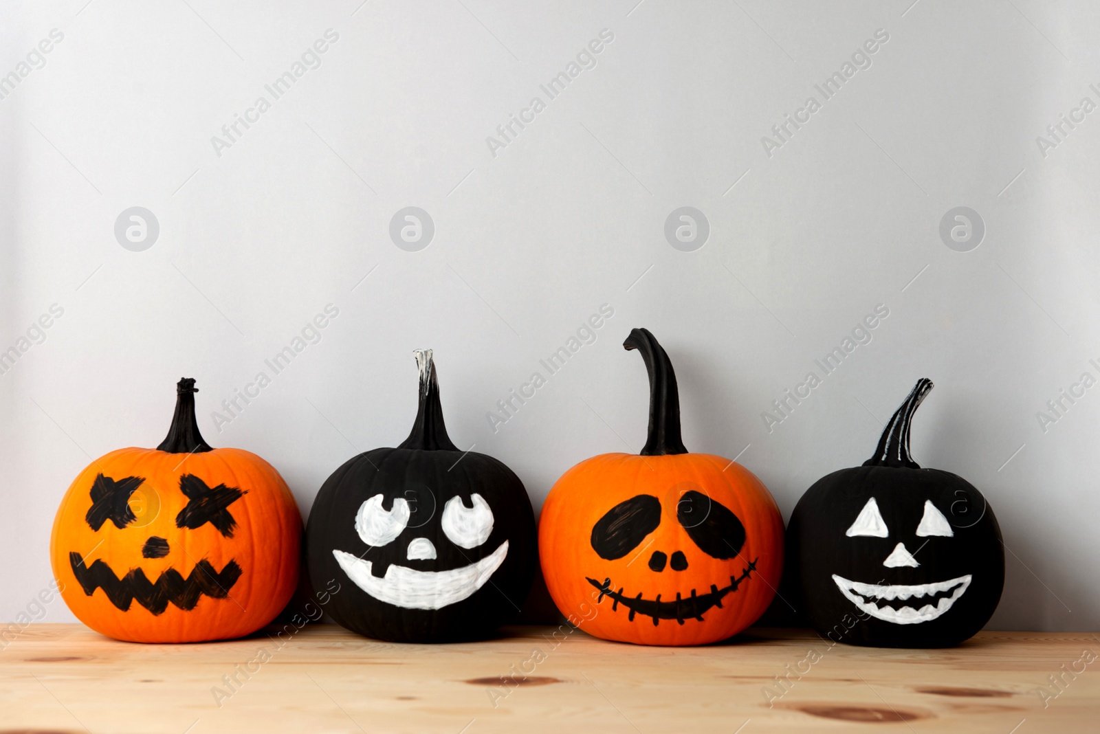 Photo of Halloween celebration. Pumpkins with spooky drawn faces on wooden table, space for text