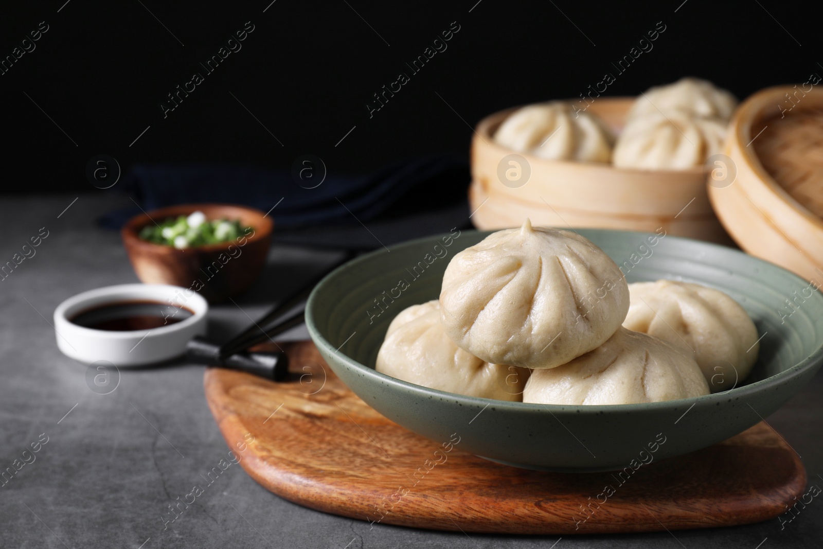 Photo of Delicious bao buns (baozi) in bowl on grey textured table, closeup