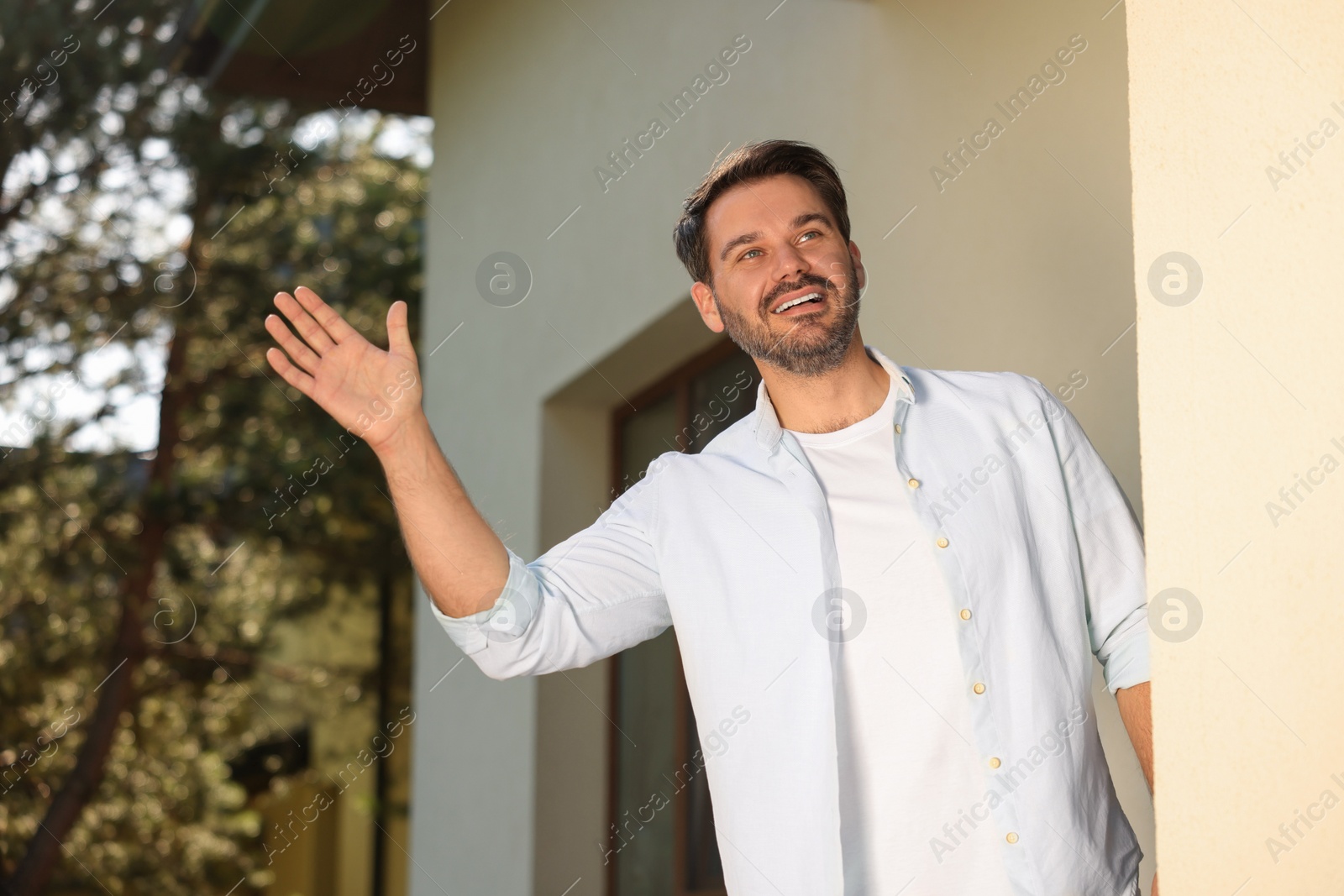 Photo of Neighbor greeting. Happy man waving near house outdoors, low angle view