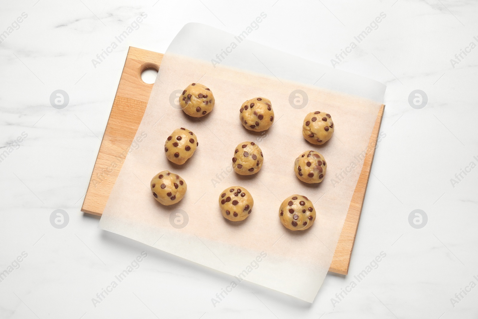 Photo of Uncooked chocolate chip cookies on white marble table, top view