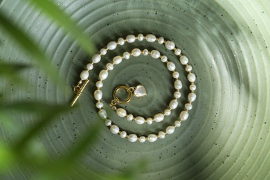 Elegant pearl necklace on olive textured background, top view