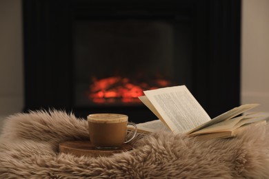 Cup of coffee and open book near fireplace at home. Cozy atmosphere