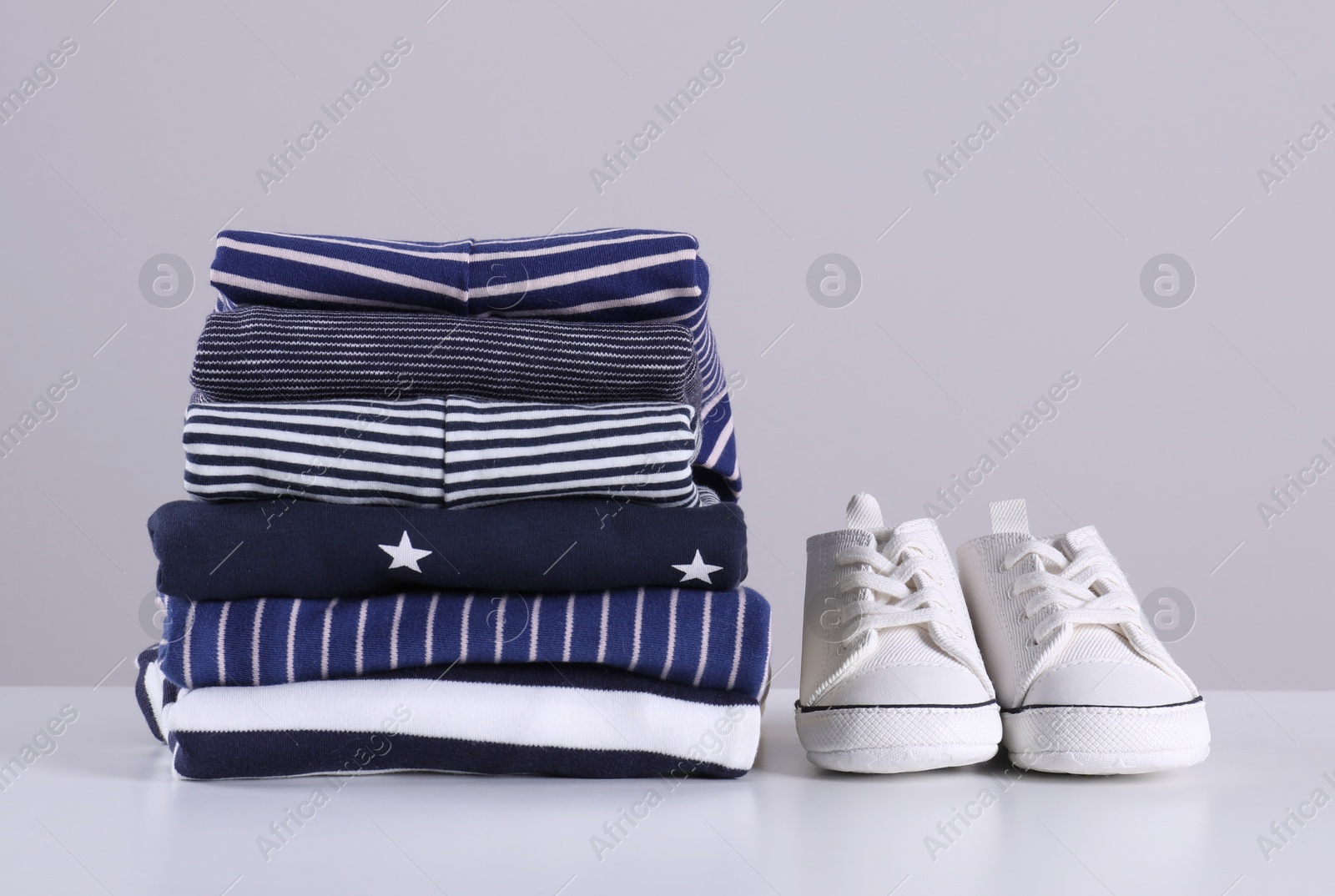Photo of Stack of clean baby's clothes and small shoes on table against light grey background