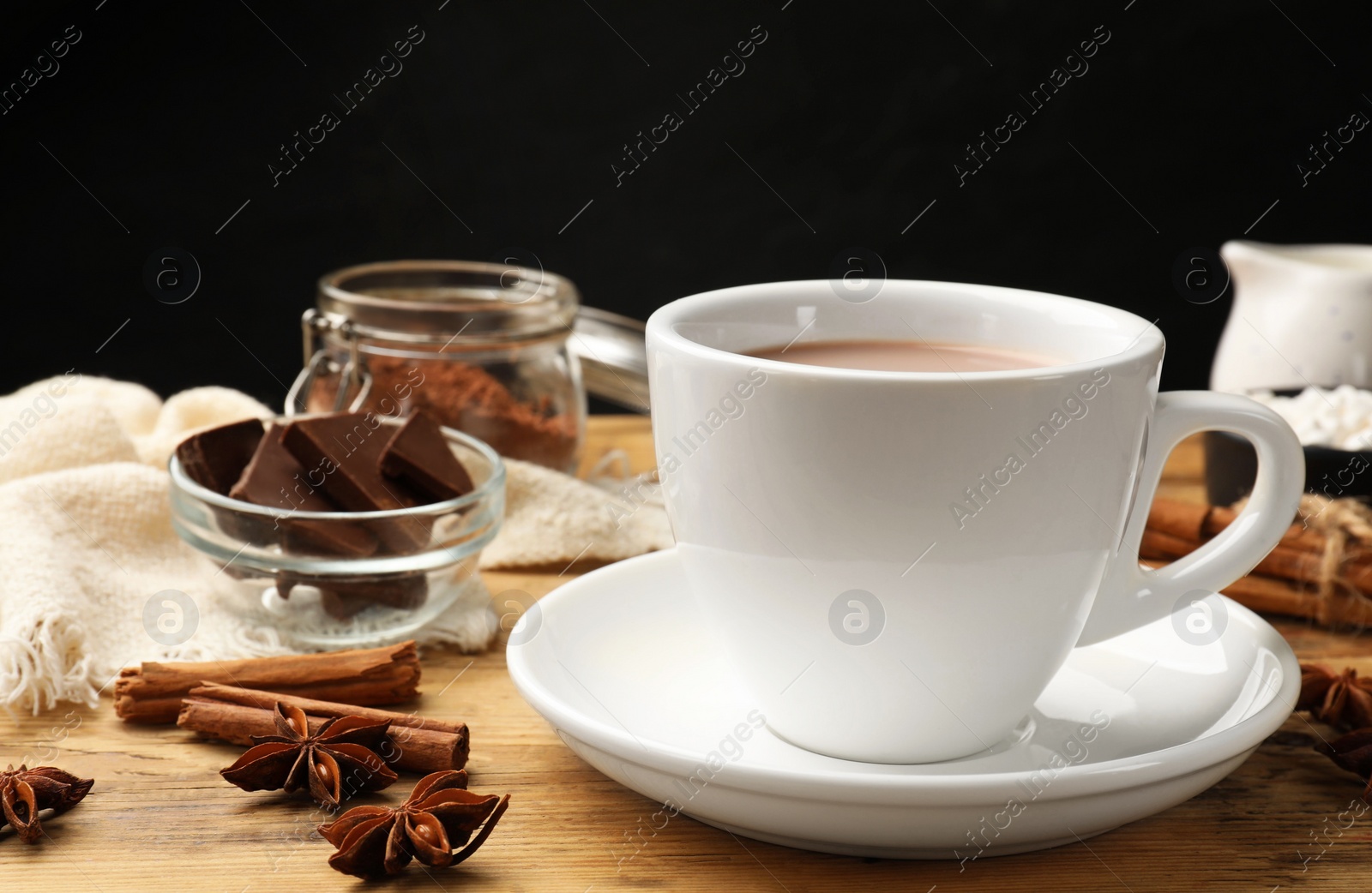 Photo of Tasty hot chocolate in cup and spices on wooden table, closeup