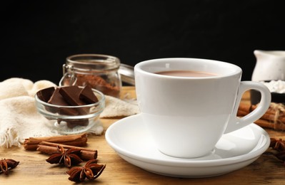 Tasty hot chocolate in cup and spices on wooden table, closeup