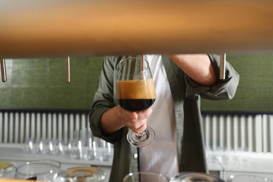 Bartender pouring fresh beer into glass in pub, closeup