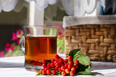 Photo of Cup of hot drink and helpful viburnum berries on white wooden table indoors