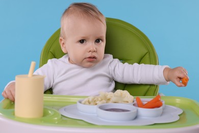 Photo of Cute little baby with healthy food in high chair on light blue background