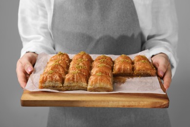 Woman with delicious sweet baklava on grey background, closeup