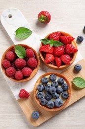 Tartlets with different fresh berries on light wooden table, flat lay. Delicious dessert
