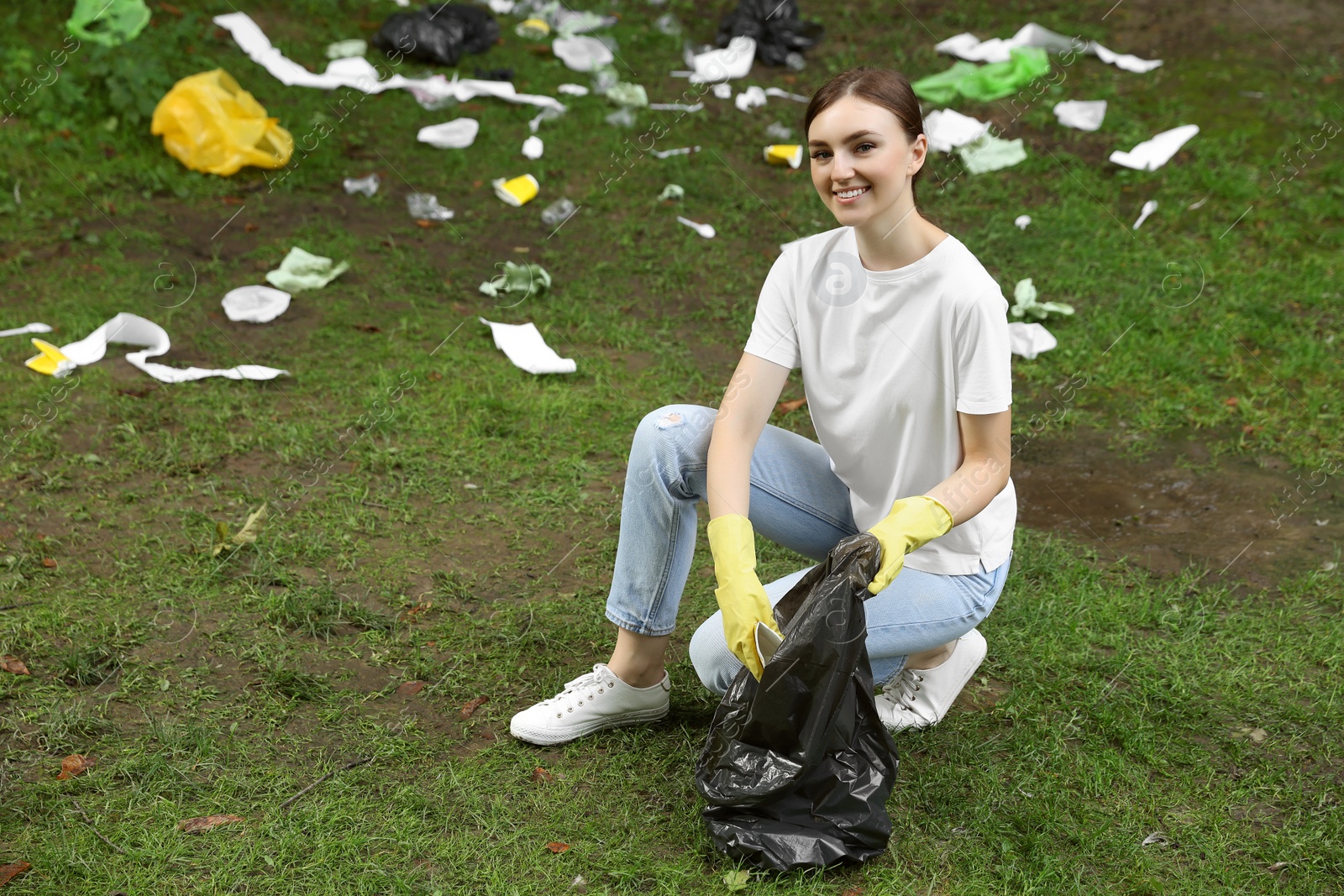 Photo of Young woman with plastic bag collecting garbage on green grass outdoors