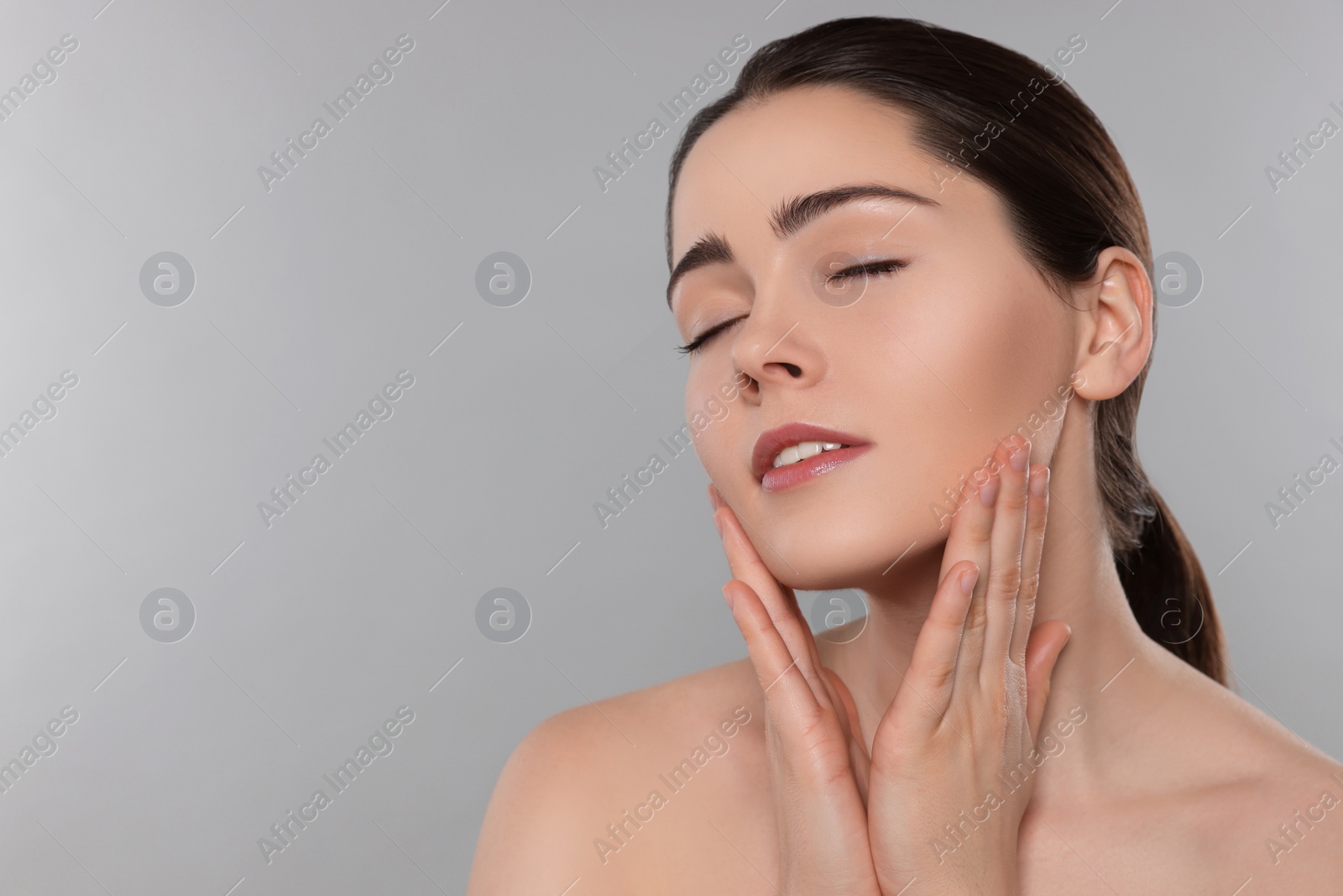 Photo of Young woman massaging her face on grey background. Space for text