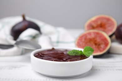Tasty sweet fig jam and fruits on white wooden table, closeup