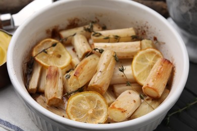 Photo of Dish with baked salsify roots, lemon and thyme on table, closeup