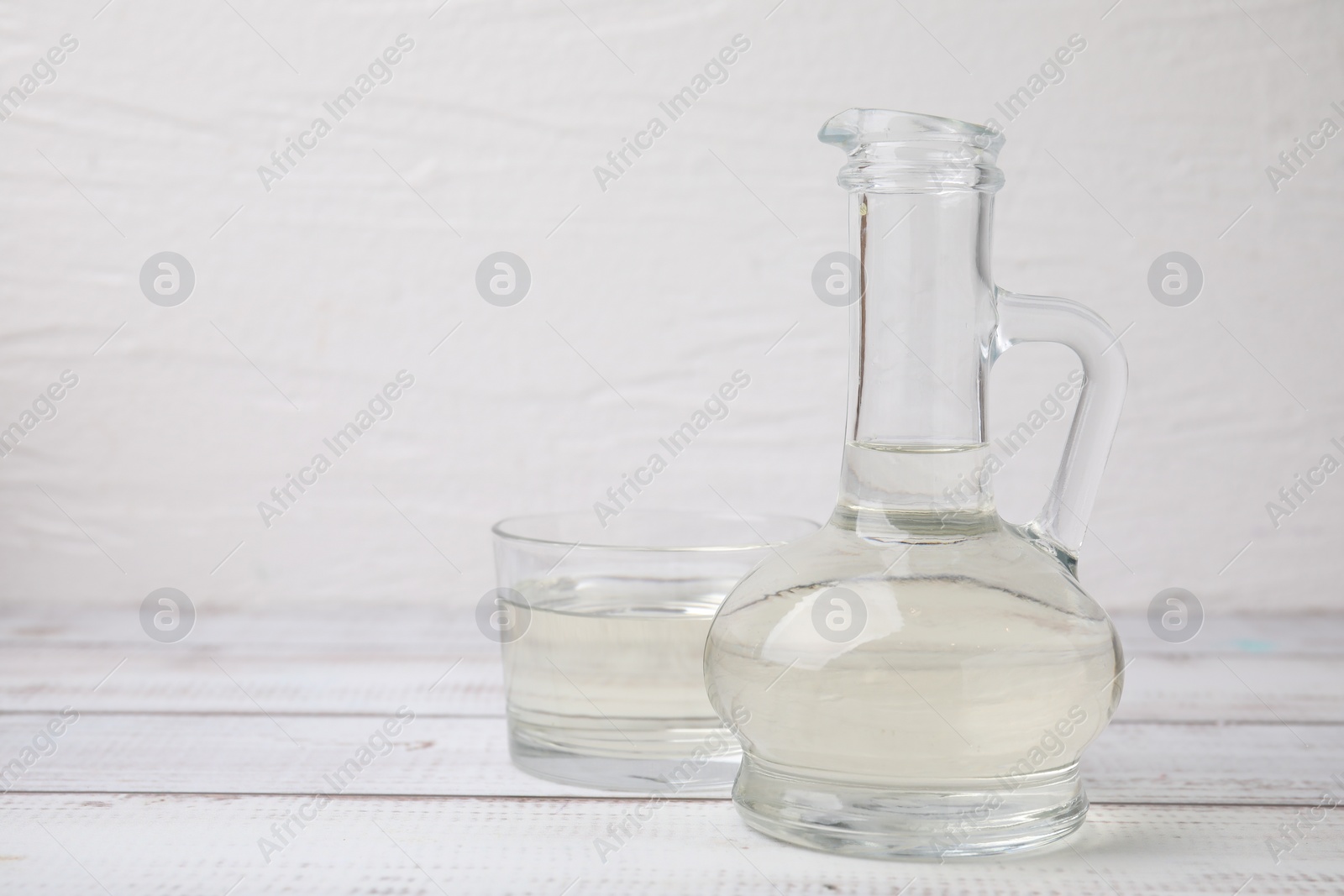 Photo of Vinegar in glass jug and bowl on white wooden table, space for text