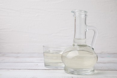 Vinegar in glass jug and bowl on white wooden table, space for text