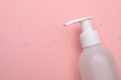 Photo of Wet bottle of face cleansing product on pink background, top view. Space for text