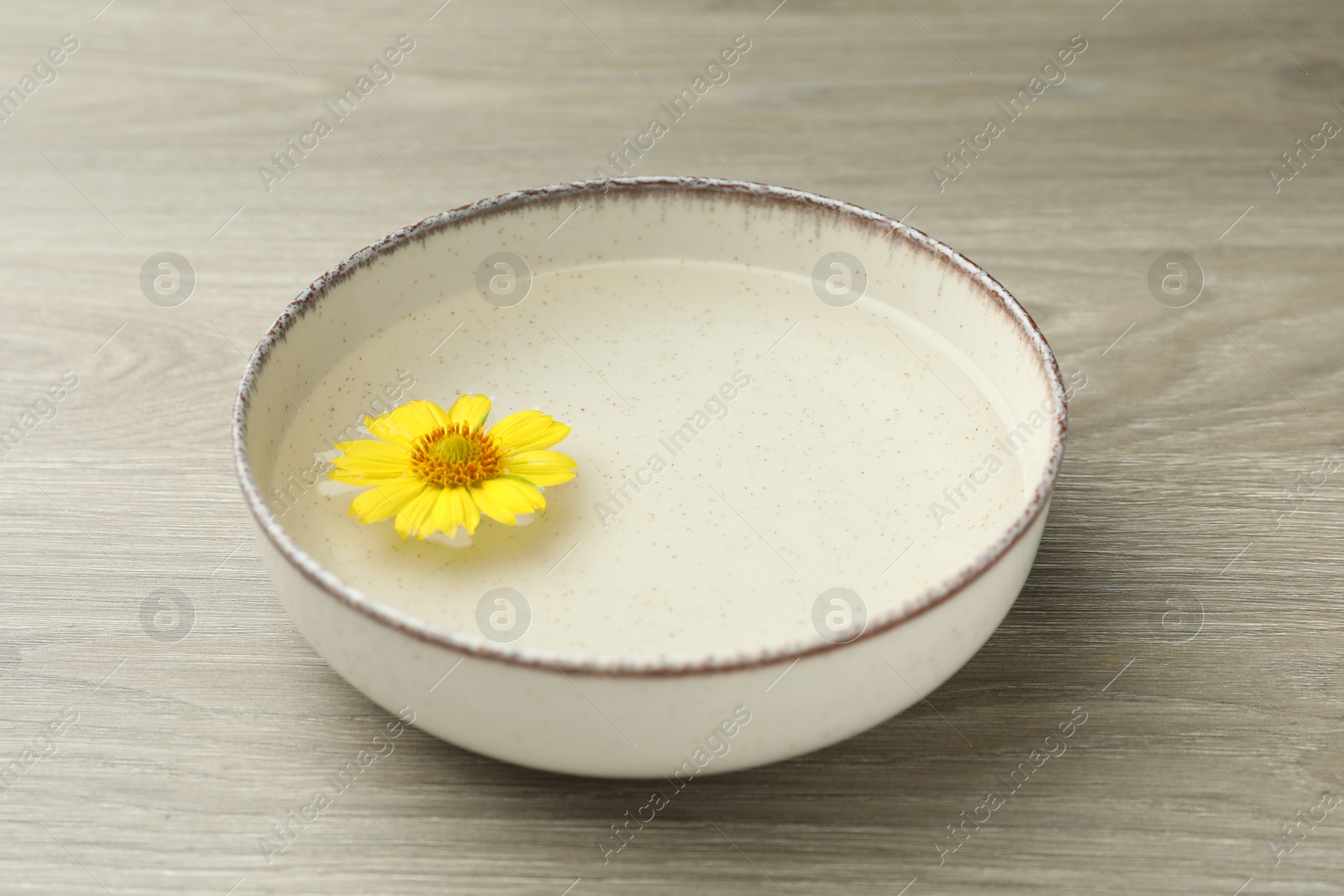 Photo of Beige bowl with water and yellow flower on wooden table, closeup